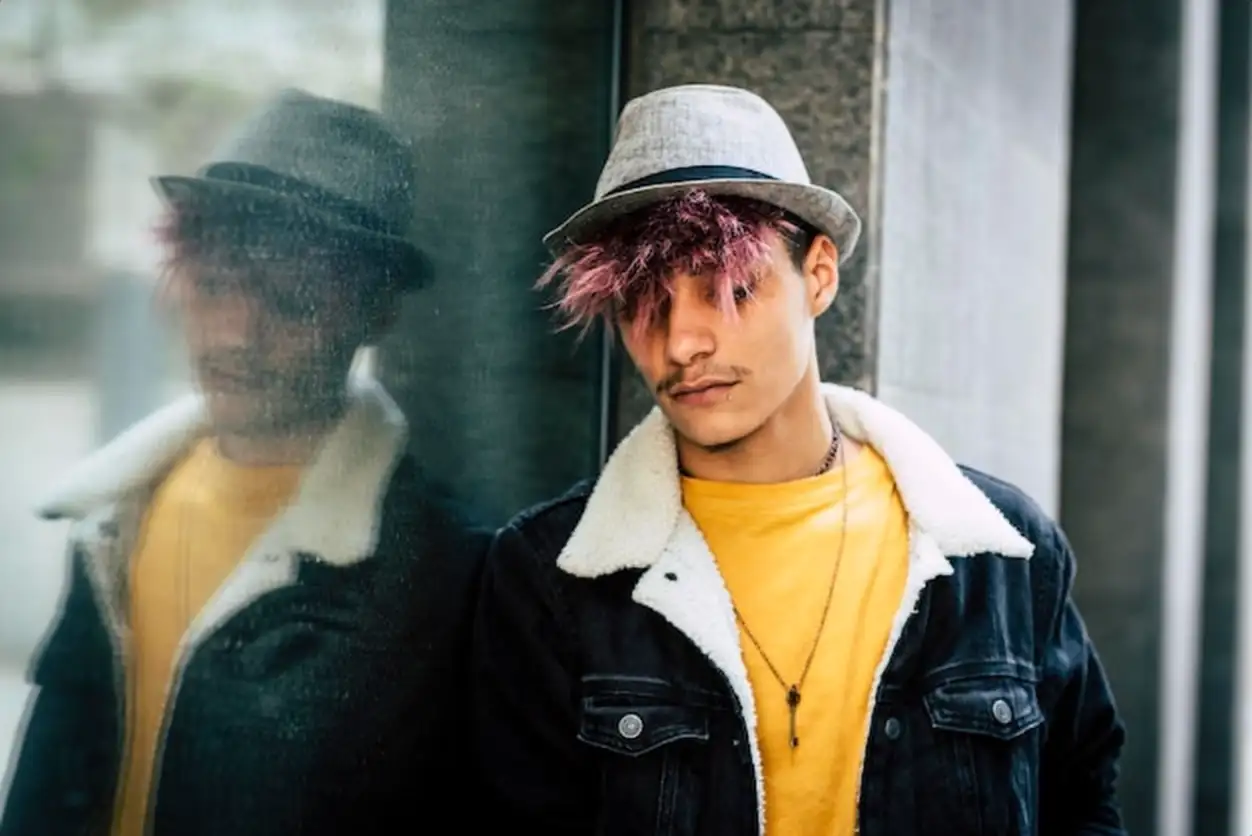 Portrait of sad young rebel teenager in the city with wall in background. Violet hair style and casual look with hat. Concept of youth people lifestyle
