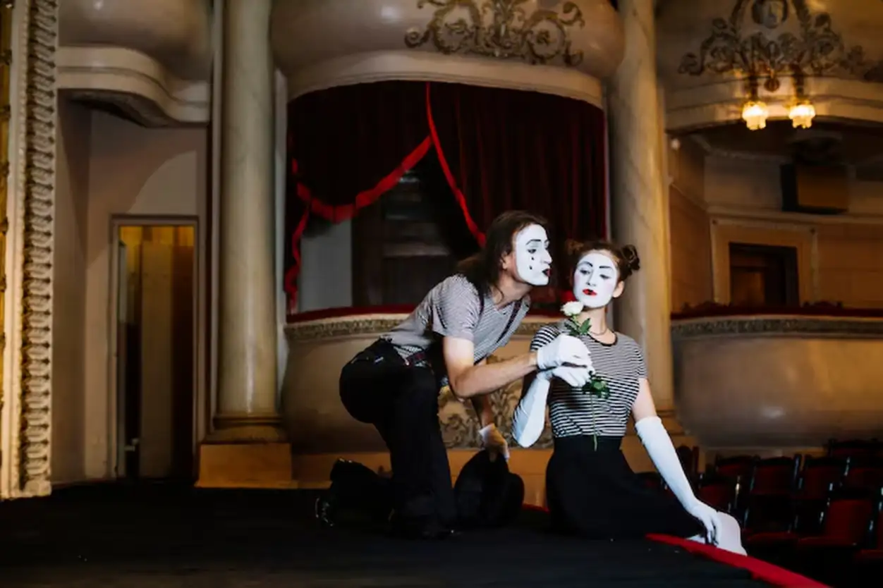 Male mime artist giving white rose to female mime sitting on stage