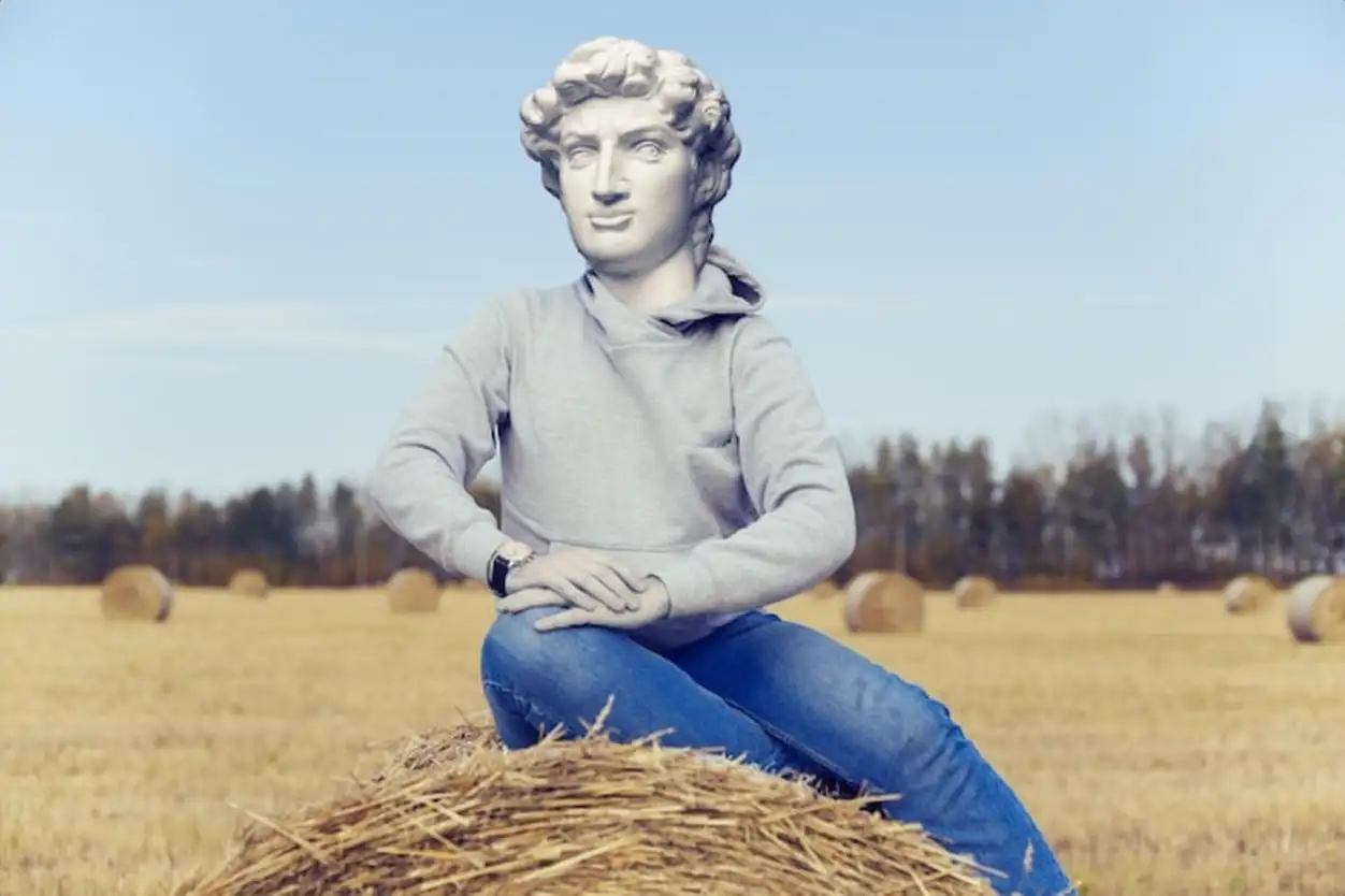 Abstract modern collage. The man with the plaster head of David in hoodie sits on a haystack