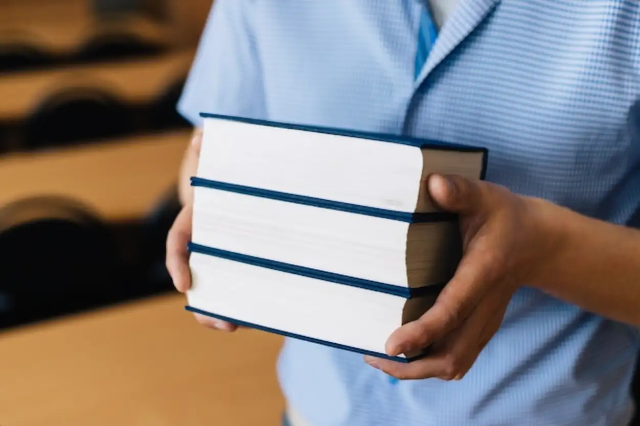 Male hands holding a stack of books.