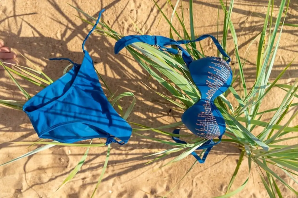 Bright blue swimwear laid among lush grass on a sandy beach