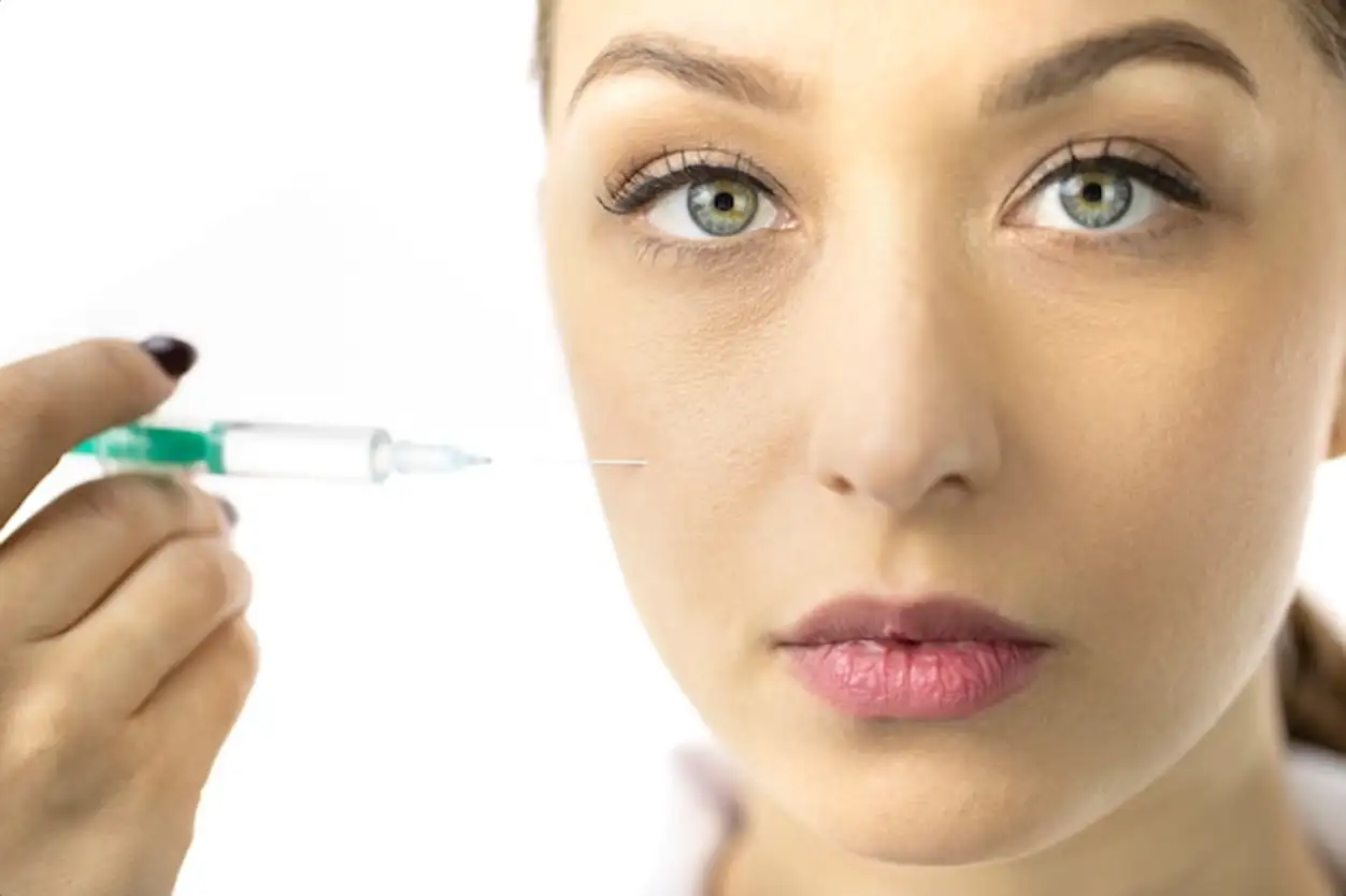 Young woman filling female wrinkles on cheek with hyaluronic acid from syringe