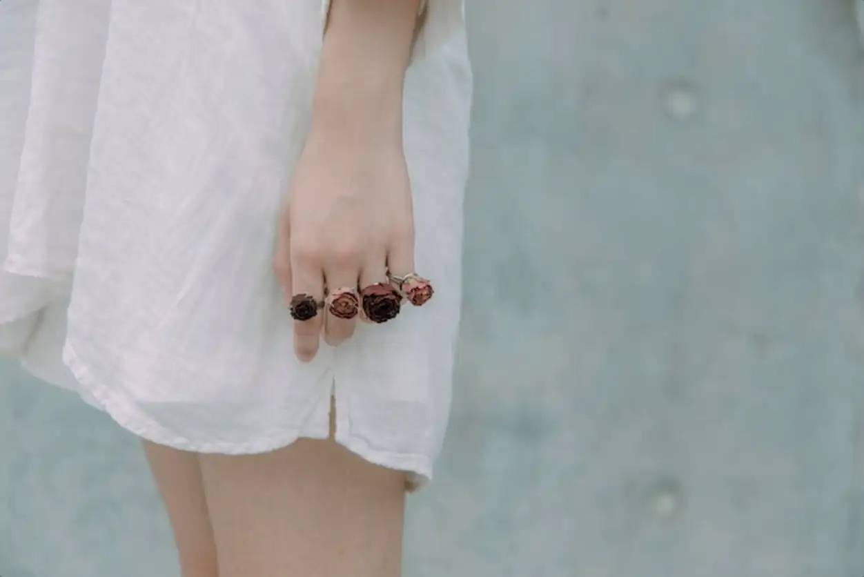 Midsection of young woman wearing rose shape rings against wall