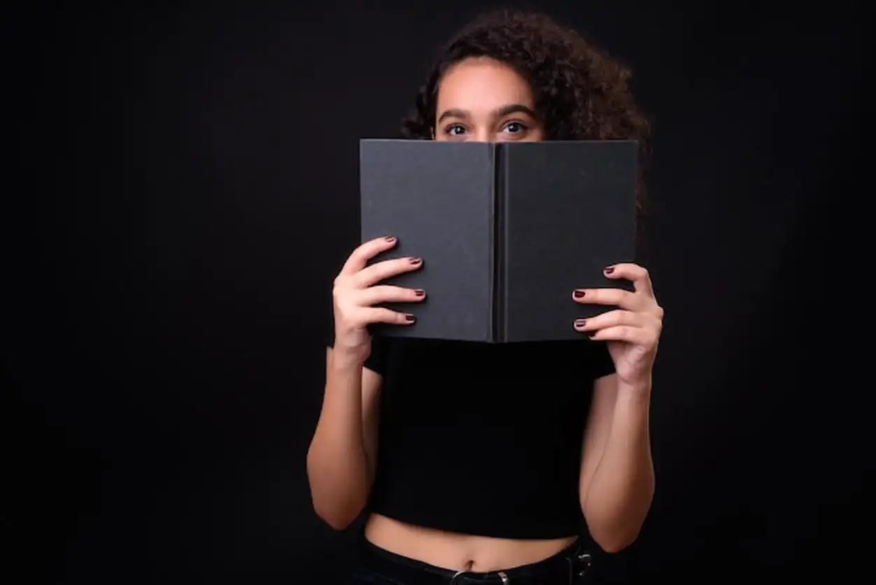 Portrait of a woman reading book against black background