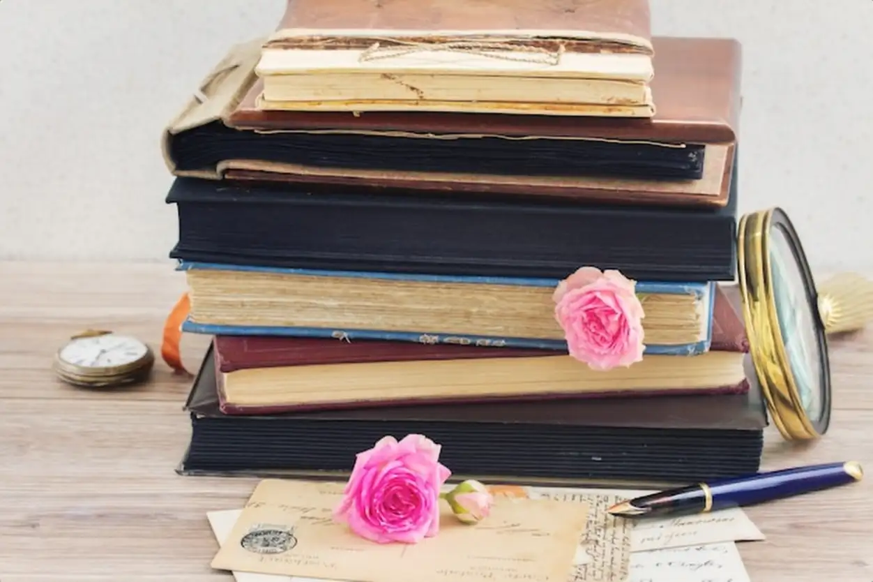 Pile of vintage old books stacked with rose buds and vintage mail on table