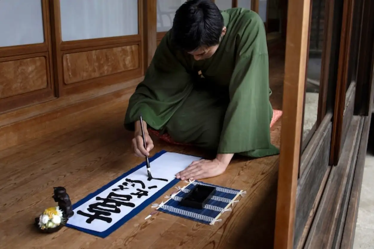 Man practicing japanese handwriting with a brush and ink