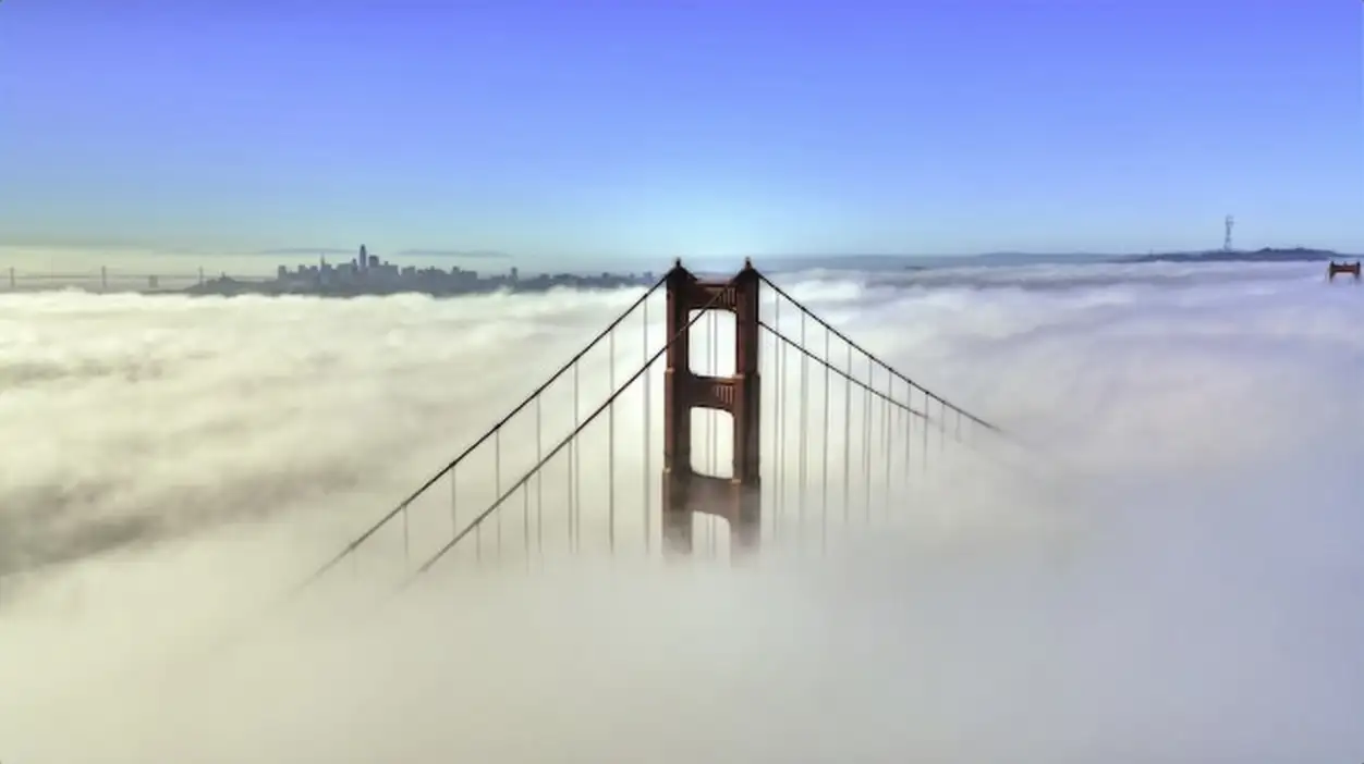 Beautiful aerial shot of the top of a bridge surrounded by clouds and blue sky