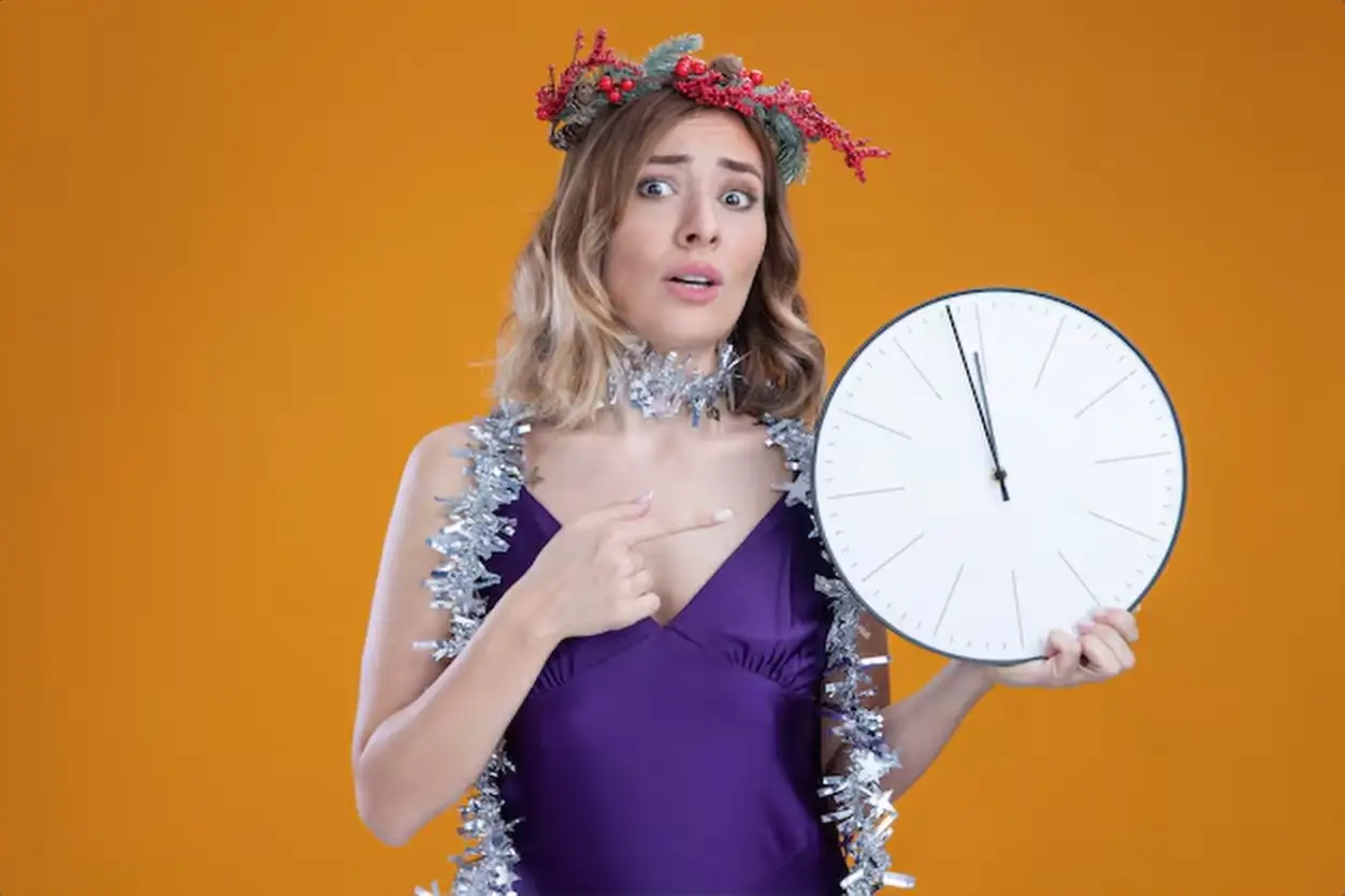 Concerned young beautiful girl wearing purple dress and wreath with garland on neck holding and points at wall clock isolated on brown background